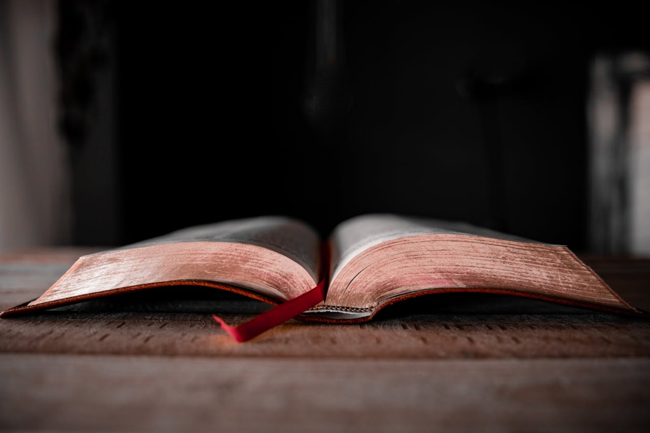 An open Bible with a red bookmark lies on a rustic wooden table.